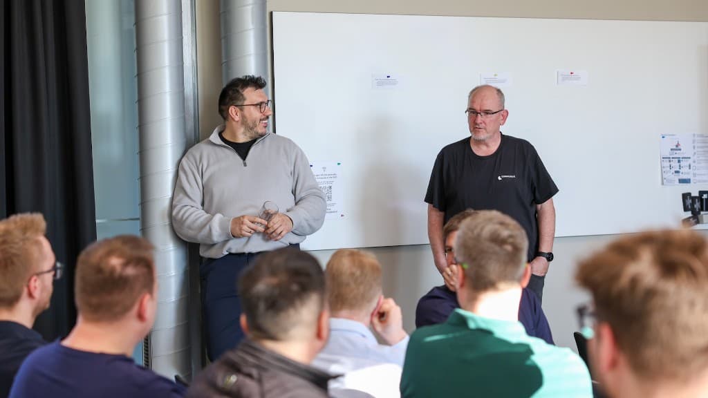 Zwei Gesprächspartner vor Whiteboard im Austausch mit dem Publikum.