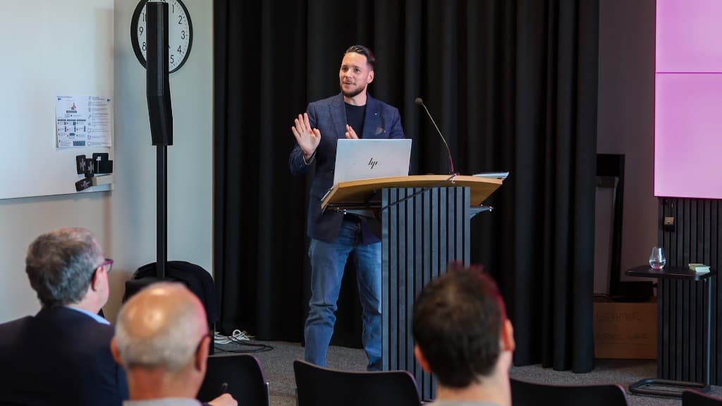 Impulsvortrag am Pult mit Laptop — Thema strategische Initiativen und Umsetzung.