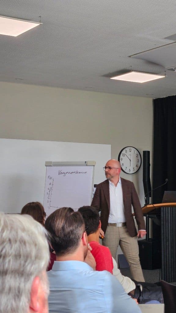 Dominik Volkert erklärt die Vergessenskurve am Flipchart vor dem Publikum.