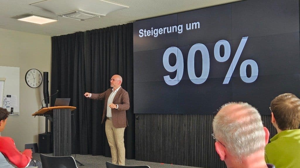 Dominik Volkert präsentiert vor einer Folie mit der Aussage „Steigerung um 90%“.