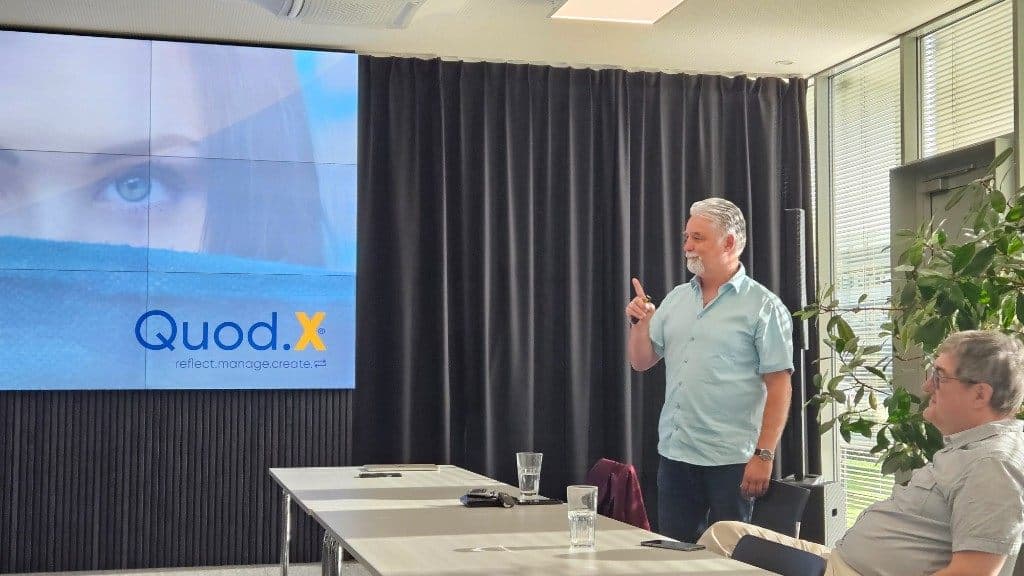 Michael Defranceschi präsentiert vor der Quod.X-Leinwand mit dem Claim „reflect.manage.create.“